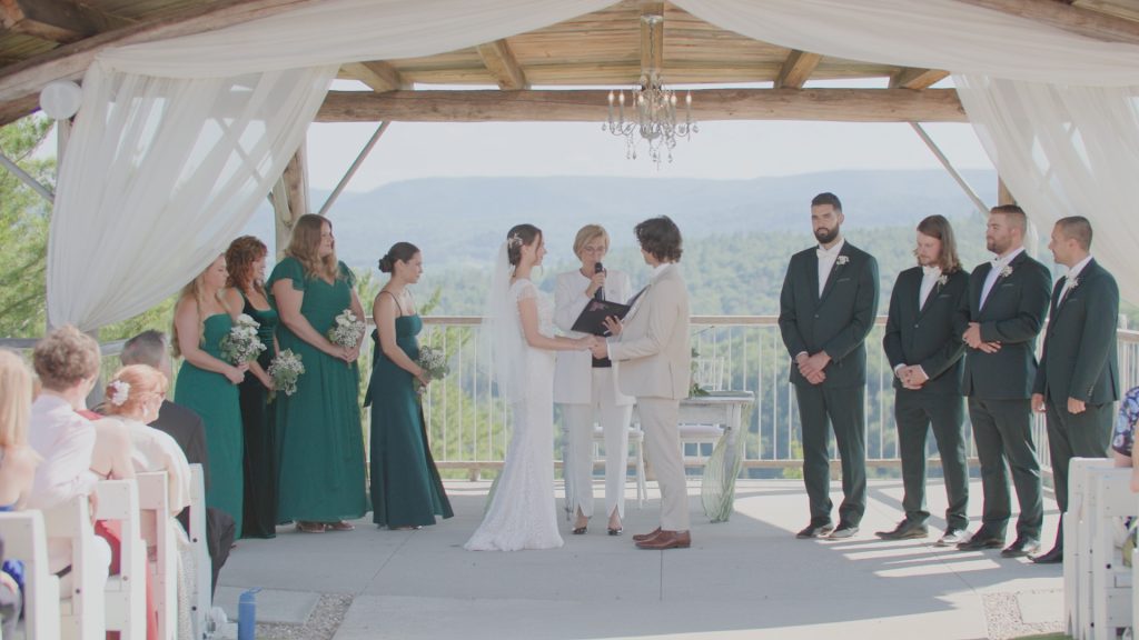 Cérémonie de mariage filmée de loin, sous une arche avec vue sur les montagnes